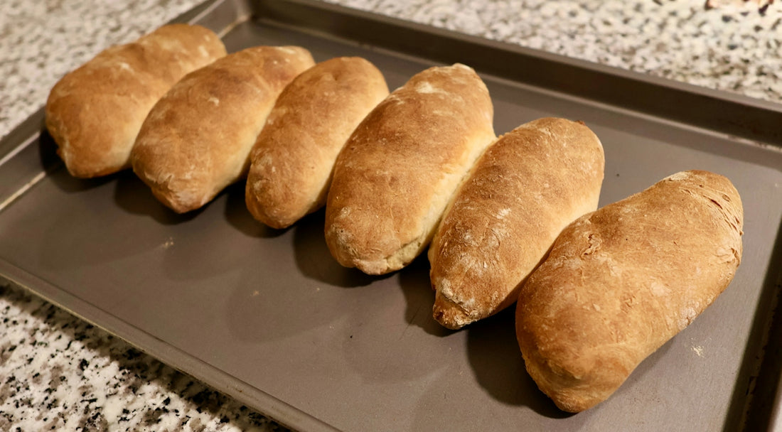 Six golden brown bread rolls on a baking sheet
