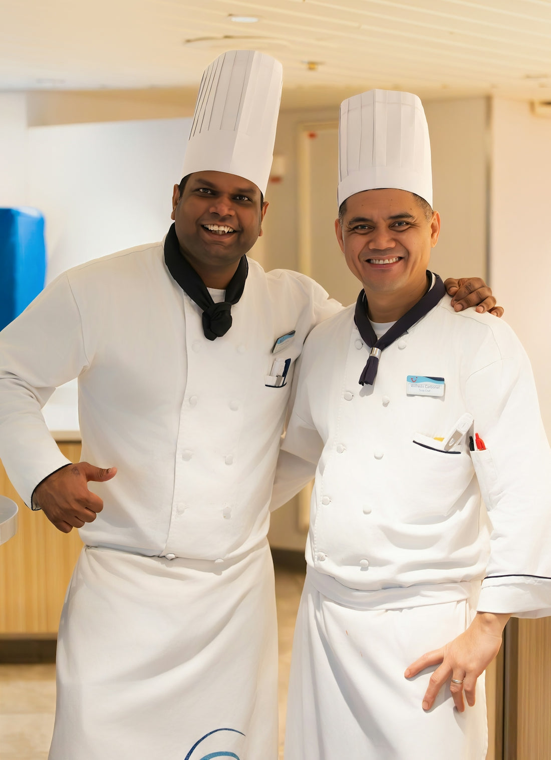 Two smiling chefs in white uniforms pose together.