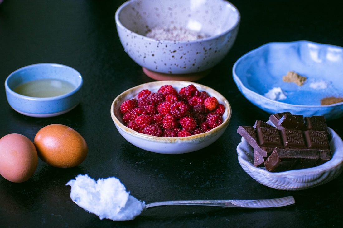 Fresh raspberries, chocolate, eggs, and other baking ingredients arranged.